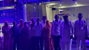 En gruppe mennesker står udenfor en bygning med et skilt, der viser 'HOTELES UNIT OF RAJ HOSPITALITY'.
