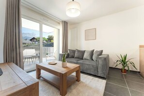 A modern living room with a sofa, a wooden coffee table, a potted plant, and a view through a sliding glass door. - Alpine - Modern 2PAX | Near train station & thermal baths | Peaceful (Saint-Gervais-les-Bains)