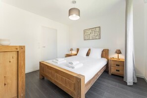 A wooden bed with white linens, a bedside table, a wall-mounted lamp, and a door. - Alpine - Modern 2PAX | Near train station & thermal baths | Peaceful (Saint-Gervais-les-Bains)