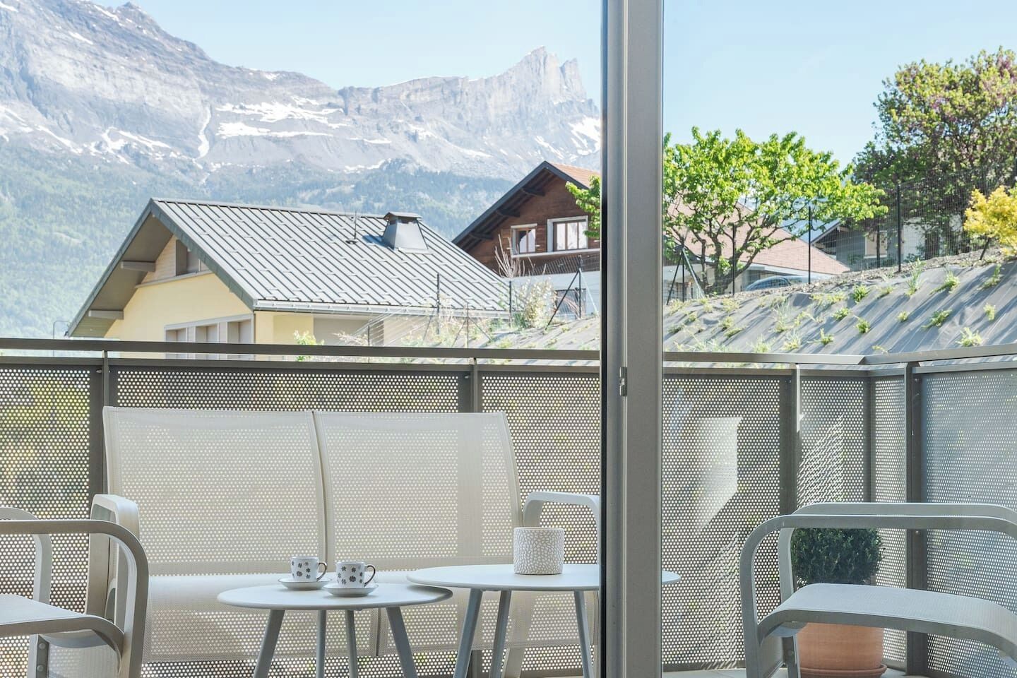 Een balkon met uitzicht op bergen, een tafel met stoelen en een glazen deur.