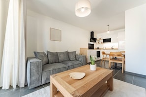 A modern living room with a grey sofa, wooden coffee table, and a kitchen in the background. - Alpine - Modern 2PAX | Near train station & thermal baths | Peaceful (Saint-Gervais-les-Bains)