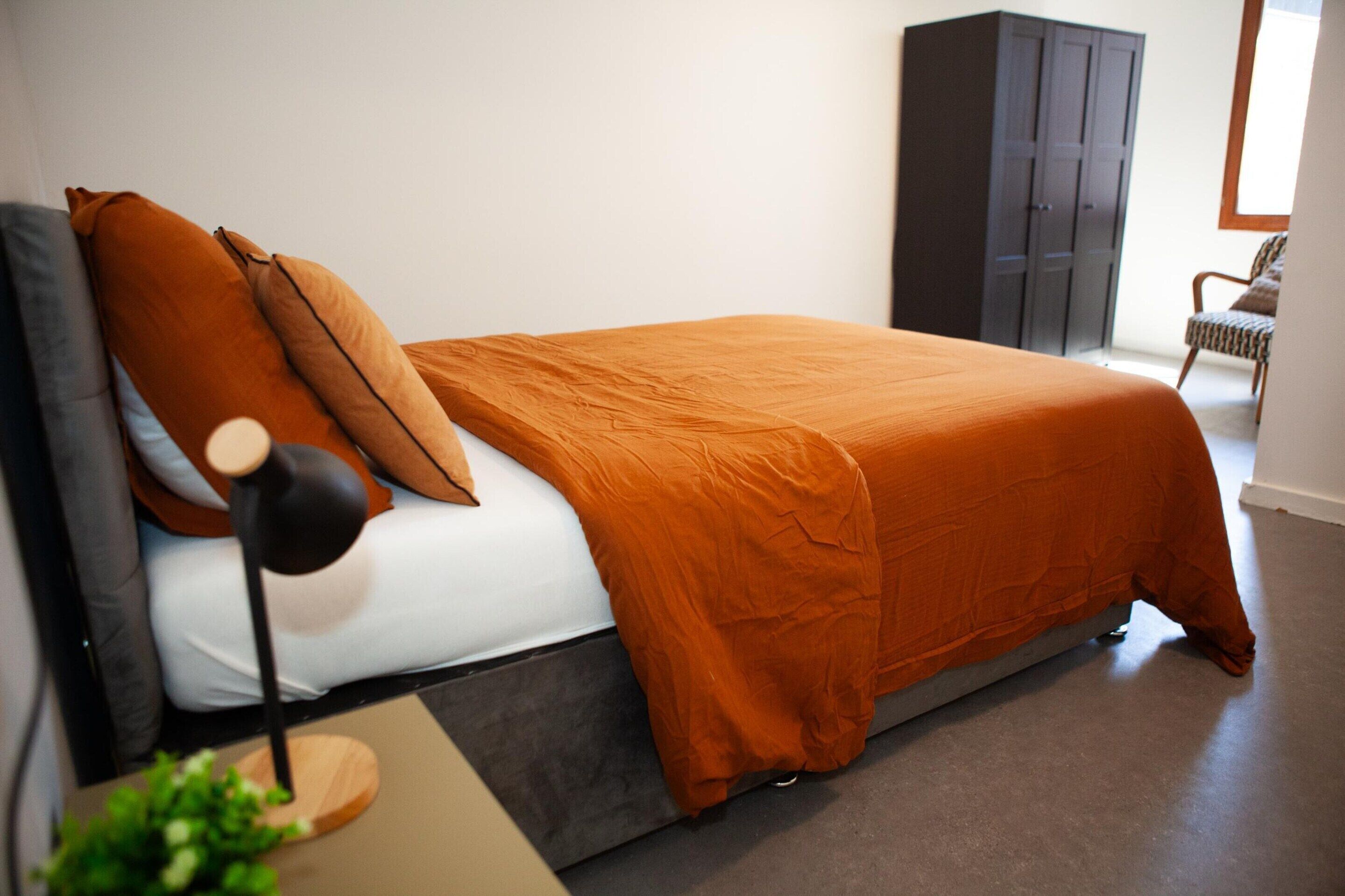 A bedroom with a bed, a nightstand, a lamp, a wardrobe, and a chair.