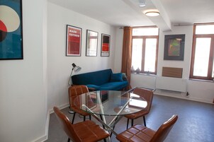 A room with a glass table surrounded by chairs, a blue sofa, and framed artwork on the walls.