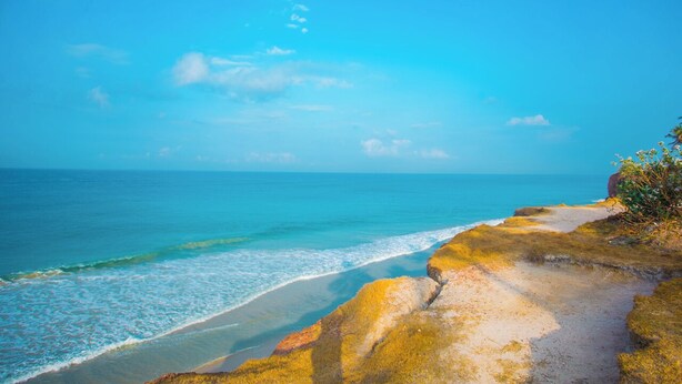 Un paisaje costero con cielo despejado, una playa arenosa y afloramientos rocosos.