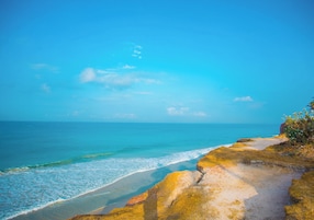 Un paisaje costero con cielo despejado, una playa arenosa y afloramientos rocosos.