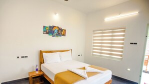 Una habitación de hotel con cama, mesita de noche, un cuadro y una ventana con persianas.