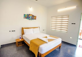 Una habitación de hotel con cama, mesita de noche, un cuadro y una ventana con persianas.