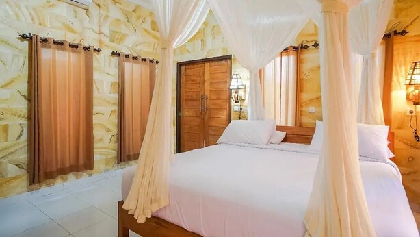 A bedroom with a four-poster bed, curtains, and a wooden door. - Mejan Beach Home Stay (Selemadeg)