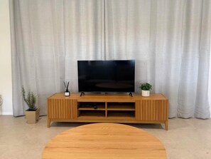 A living room with a wooden entertainment unit, a flat-screen TV, a round coffee table, and two potted plants. - Modern Sunlit Home | Spacious & Stylish Stay! (Capalaba)