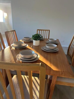 A dining table set with plates and bowls, surrounded by wooden chairs. - Modern Sunlit Home | Spacious & Stylish Stay! (Capalaba)
