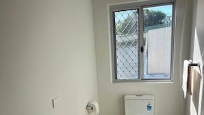 Et lille, moderne badeværelse med en hvid vask, kommode i træ, toilet og et vindue med udsigt til et hegn.