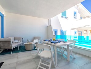 Ein Balkon mit Esstisch für zwei Personen, einer Couch und einem kleinen runden Tisch mit einer Flasche und Gläsern.
