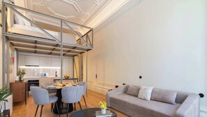 Ein modernes Wohnzimmer mit einer Couch, Esstisch, Stühlen und einer Treppe, die in eine obere Etage führt.