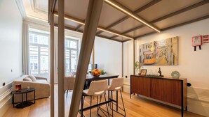 Ein modernes Wohnzimmer mit einer Couch, einem Essbereich mit Tisch und Stühlen, einem Holzschrank und einem Gemälde an der Wand.