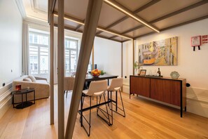 Ein modernes Wohnzimmer mit einer Couch, einem Essbereich mit Tisch und Stühlen, einem Holzschrank und einem Gemälde an der Wand.