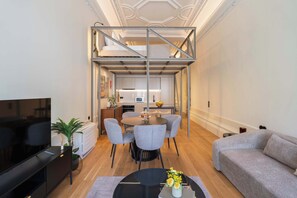 Ein modernes Wohnzimmer mit Fernseher, Sofa, Esstisch und Stühlen.