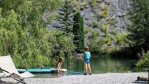A lakeside setting with a paddleboard, a lounge chair, and a rocky hillside.