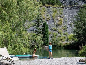 A lakeside setting with a paddleboard, a lounge chair, and a rocky hillside.