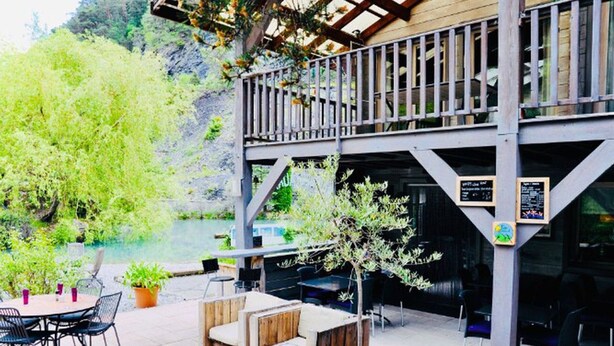 An outdoor patio with tables and chairs, a wooden deck, and a view of a natural landscape.
