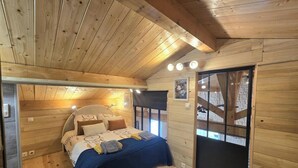 Ein Schlafzimmer einer Holzhütte mit Bett, Kissen, Decke, Fenster und Tür.