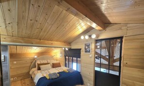 A wooden cabin bedroom with a bed, pillows, a blanket, a window, and a door. - House with AC, pets welcome - 6 guests (Lalinde)