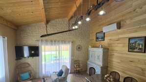 Ein rustikaler Raum mit Steinwand, Holzbalkendecke, Kamin, Fernseher und Essbereich.