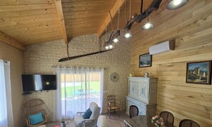 A rustic room with a stone wall, wooden ceiling beams, a fireplace, a television, and a dining area. - House with AC, pets welcome - 6 guests (Lalinde)