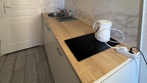 Et kompakt køkken med en væg i natursten, en vask, en bordplade med elkedel og et billede over skabene.