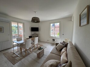 Ein großzügiges Wohnzimmer mit einer Couch, einem Esstisch und Stühlen. An der Wand ist ein Fernseher angebracht, und ein Fenster bietet einen Blick ins Freie.