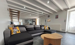 Una sala de estar moderna con un sofá modular, una mesa de centro de madera y una cocina al fondo.