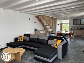 Un salon moderne avec un canapé d’angle, une table basse en bois et un escalier menant à un espace repas.