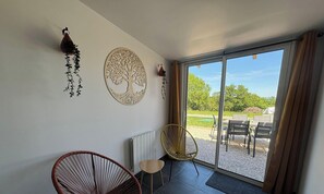 Habitación con puerta de cristal corredera que da a un espacio exterior, un radiador, dos sillones de mimbre y adornos en la pared.