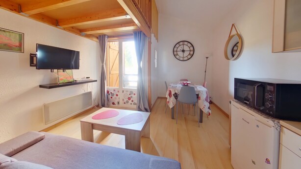 A room with a bed, a TV, a small table, a chair, a clock, and a refrigerator.