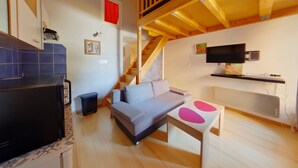A compact living space with a sofa, a small table, a television, a staircase, and a kitchen area.