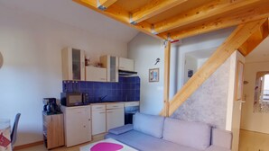 A compact living space with a kitchenette, a sofa, a small table, and a staircase.