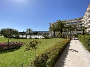 A pathway leading to a building with multiple balconies, surrounded by well-maintained grass and palm trees. - Bright apartment, park view - 4 guests (Juan les Pins)
