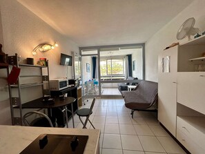 A compact kitchen with a dining area, a sofa, and a TV mounted on the wall. - Quiet studio, garden view - 4 guests (Cap d'Agde)