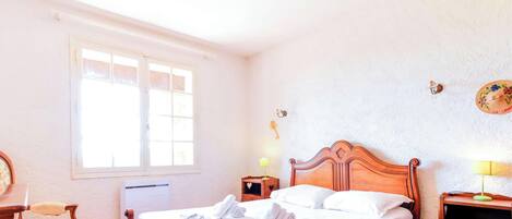 A bedroom with a wooden bed, a window, a radiator, a bedside table with a lamp, and a wall-mounted clock.