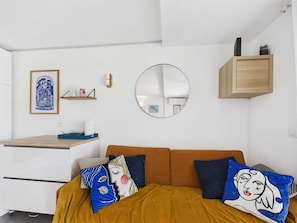 A modern bedroom with a bed, a round mirror, a wooden shelf, and a framed artwork on the wall. - Apartment with AC and WiFi - 5 guests - In the village center (Le Grau d'Agde)
