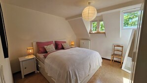 Un dormitorio con cama, lámparas de noche, un radiador, una ventana y una silla.