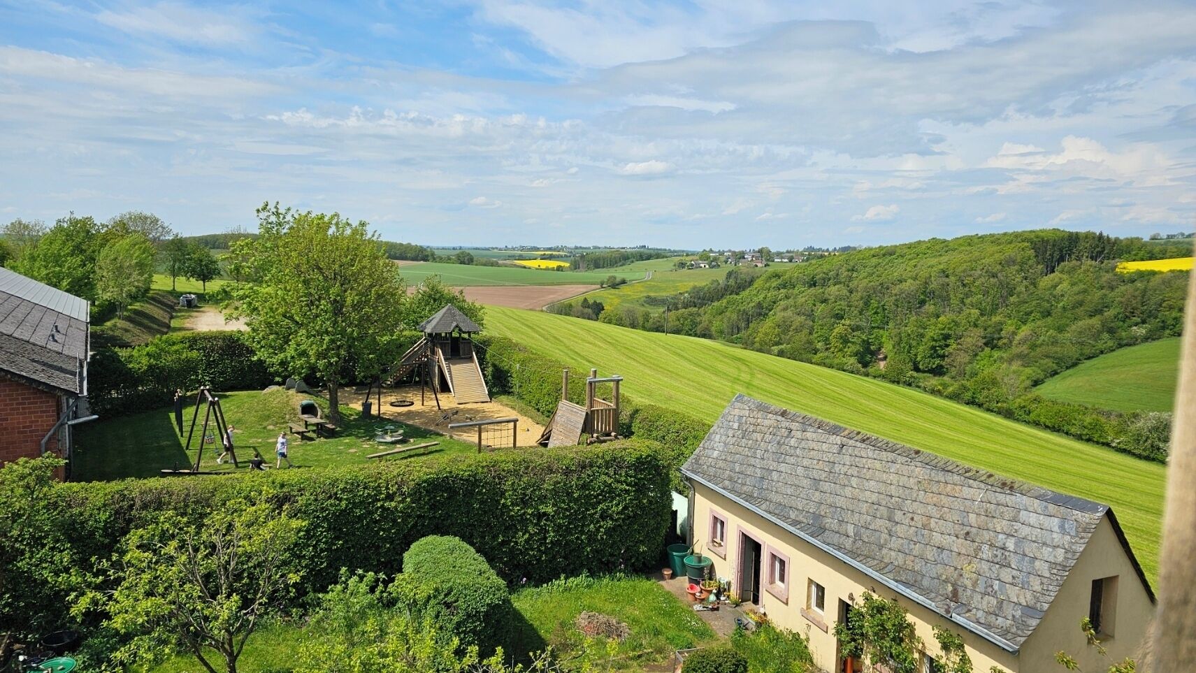 Ländliche Landschaft mit einem Haus, einem Spielplatz und grünen Feldern.