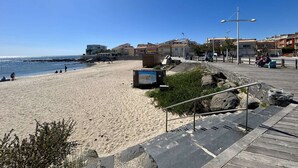Ein Strand mit einer Holzpromenade, einem Felsen und Gebäuden im Hintergrund.