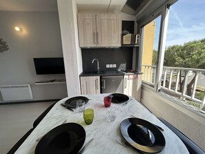 A compact kitchen with a microwave, a small refrigerator, and a dining area with a table set for two. - Studio with cabin & parking - Cap d'Agde - 4 guests (Cap d'Agde)
