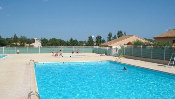 Ein Schwimmbecken mit klarem, blauem Wasser, umgeben von einer gefliesten Terrasse und einem Zaun.