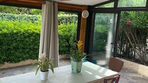 Ein Wintergarten mit Tisch und Stühlen, Blumentöpfen, einer Hängelampe und einer Wanduhr.