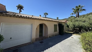 A single-story house with a white garage door, a small entrance with a green door, and a tiled roof. - Quiet villa with air conditioning and pool (Cavalaire-sur-Mer)