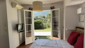 A bedroom with a bed, a television, and a view of a garden and mountains. - Quiet villa with air conditioning and pool (Cavalaire-sur-Mer)
