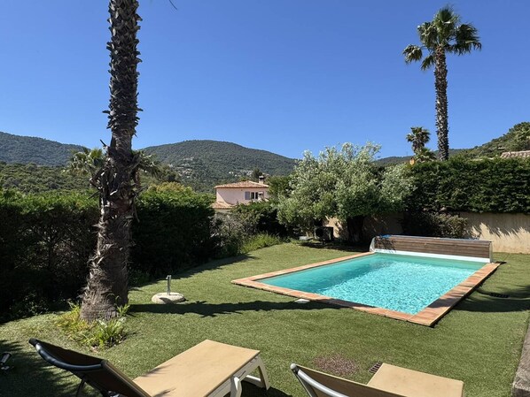 Ein Swimmingpool mit Blick auf einen Berg, umgeben von Palmen und einem kleinen Gebäude.