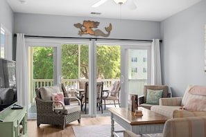 Ein Wohnzimmer mit einem großen Schiebeglasfenster, das auf eine Terrasss führt, einem Deckenventilator und einem dekorativen Wandbild einer Meerjungfrau.