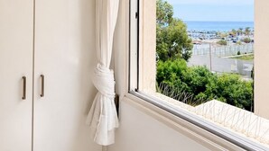 Ein Zimmer mit Fenster, Vorhang und Blick auf das Meer und Gebäude.